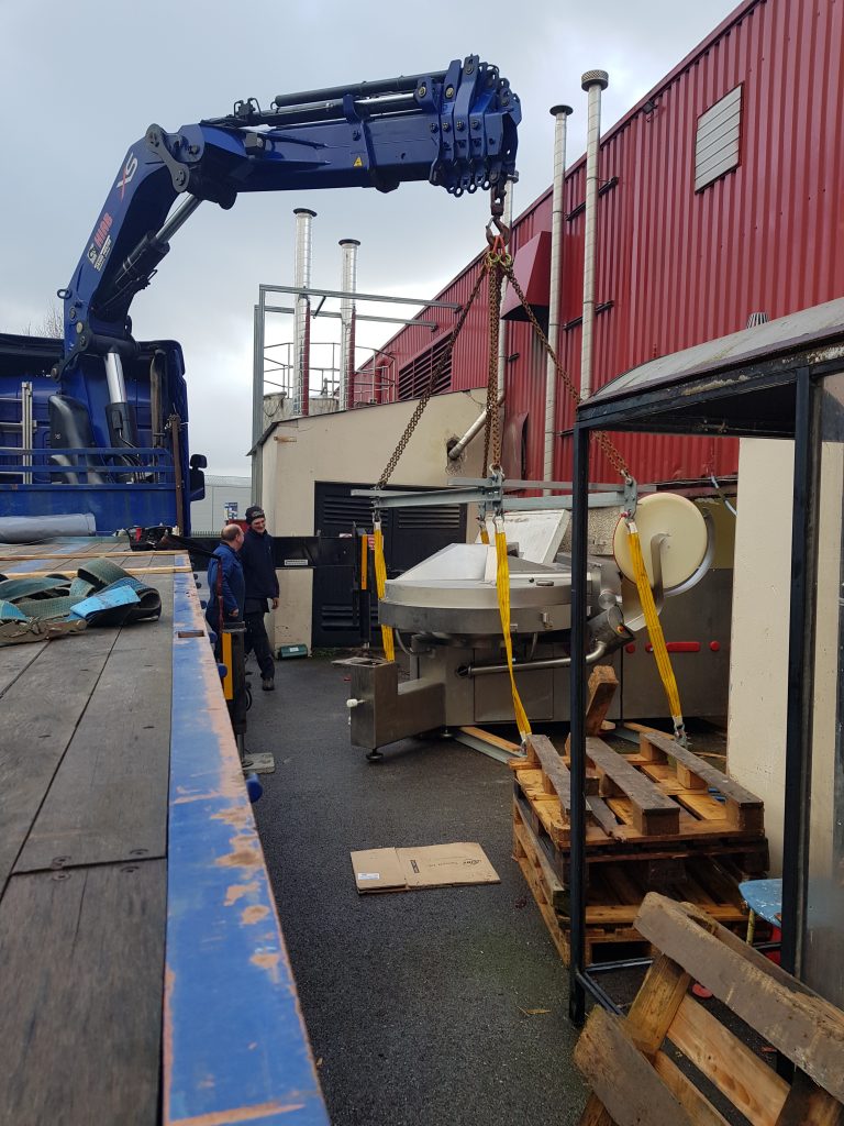 workers looking at a truck mounted crane loading item into a factory